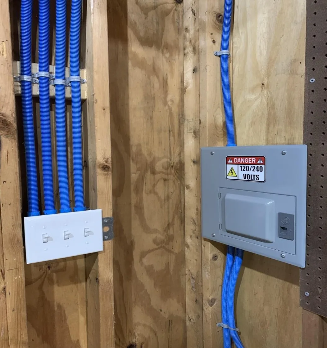 Blue wiring runs strapped straight down a framed wall to a small panel and a triple switch plate