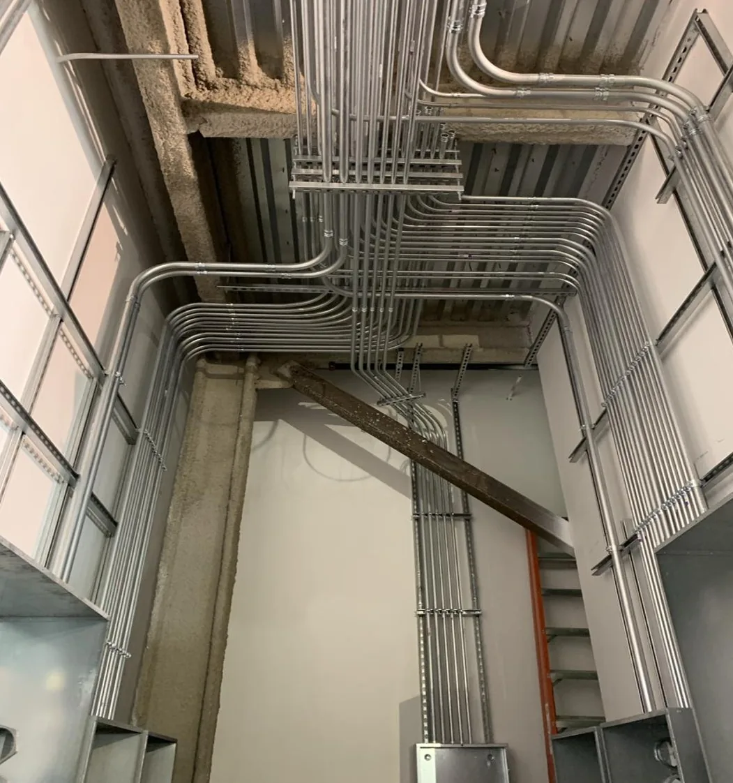 Parallel runs of EMT conduit bent around the ceiling and down the walls of a tall commercial room