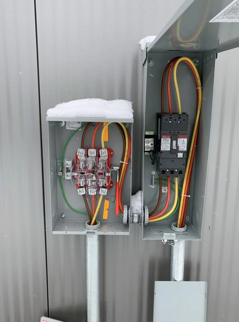 An open meter socket and disconnect on a pedestal, wired with color-coded conductors